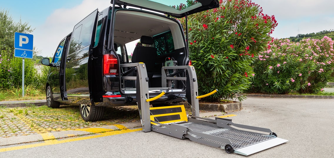 Black luxury wheelchair-accessible van with hydraulic lift deployed at ADA parking spot